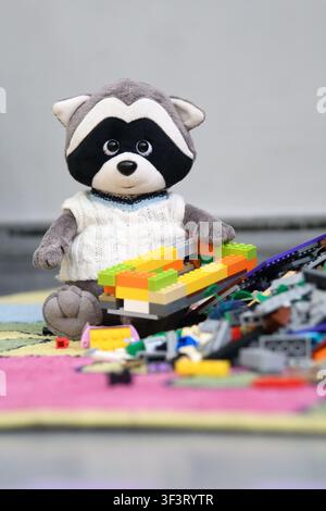 Cute plush raccoon building colorful toy bricks on the playroom floor. Сonstruction set. Stock Photo