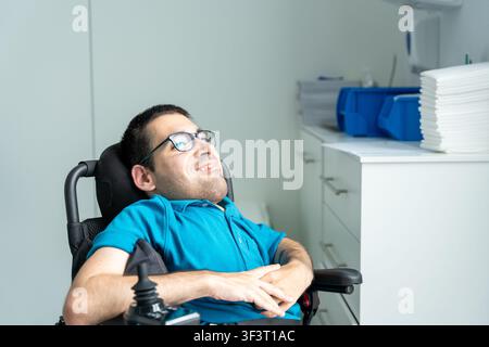 Young man with a disability smiling in an electric wheelchair inside a clinic office Stock Photo