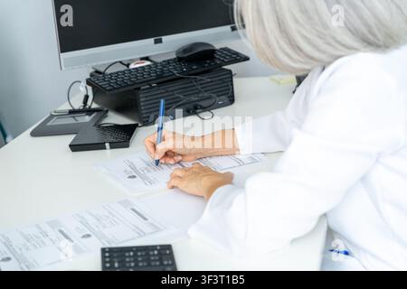 Doctor hands writing patient medical data on official documents at desktop Stock Photo