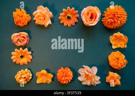 A flat composition featuring a frame made up of decorative flowers in shades of oran-ge and peach on a green background. Stock Photo