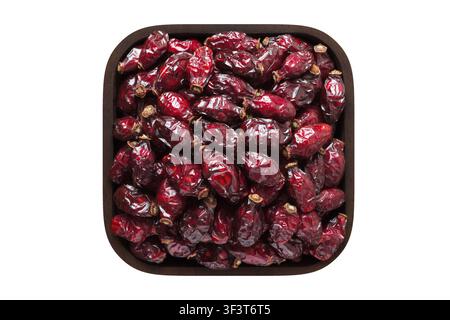 dried rose hips or dogrose berries in wooden bowl closeup. vegetarian food isolated on white. Stock Photo