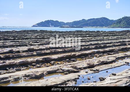 A scenic coastal landscape featuring distinctive geological rock formations in the foreground, characterized by parallel ridges and grooves creating Stock Photo