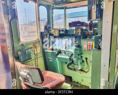 Interior view of a vintage Japanese train driver's cabin featuring green painted control panels and machinery. The cockpit contains an orange Stock Photo