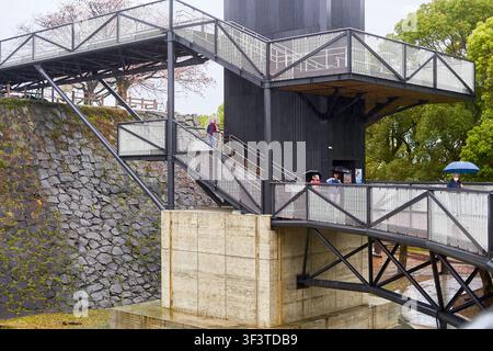 Modern steel and concrete elevated walkway and elevator structure attached to a historic Japanese castle stone wall. The architectural installation Stock Photo