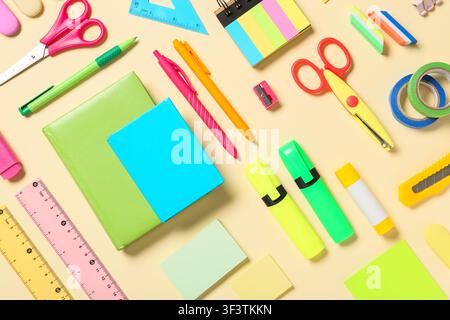 Colorful school and office supplies including notebooks, pens, scissors, and highlighters on a light yellow background Stock Photo