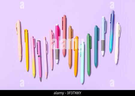 Colorful ballpoint pens in various shades of pink, orange, green, and blue arranged on a light purple background Stock Photo