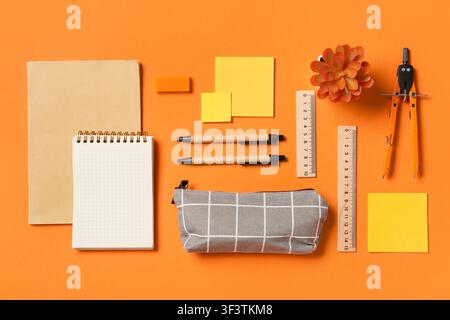School supplies and stationery items including notebooks, pens, rulers, and a compass on an orange background Stock Photo