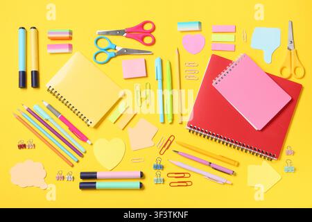 Colorful school and office supplies including notebooks pens pencils and scissors arranged on a bright yellow background Stock Photo