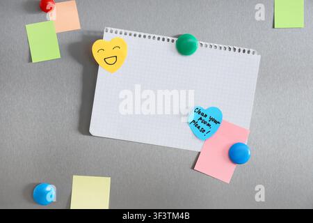 Blank grid paper notebook page with colorful sticky notes and magnets on a brushed metal refrigerator door, Various sticky notes in different colors a Stock Photo