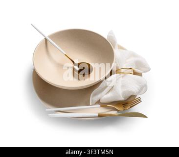 Modern beige ceramic dinnerware set with gold and white cutlery, napkin, and napkin ring, isolated on a white background Stock Photo