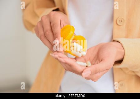 Womans hands pouring white capsules from a yellow prescription bottle into her palm, health and wellness Stock Photo