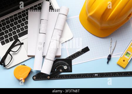 Architectural blueprints and construction tools with a laptop and hard hat on a light blue background, top view Stock Photo