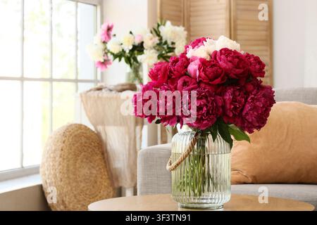 Lush bouquet of deep pink and white peonies in a ribbed glass vase on a wooden table in a bright living room, the setting is a bright living room, a s Stock Photo