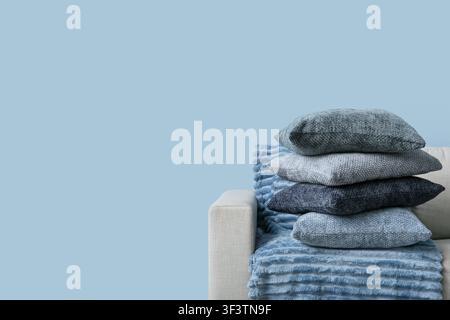 Stack of blue and gray decorative pillows on a beige sofa with a soft blue blanket, home decor and comfort Stock Photo