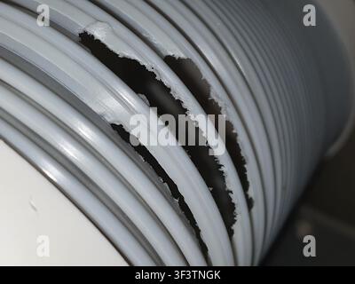 Macro close-up view of a damaged white plastic corrugated hose or flexible tube showing multiple longitudinal splits and tears along the spiral Stock Photo