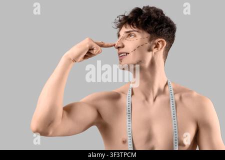 Young man with markings on his face and tape measure against grey background, closeup. Plastic surgery concept Stock Photo