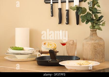 Dirty dishes and frying pan on wooden counter near beige wall in kitchen Stock Photo