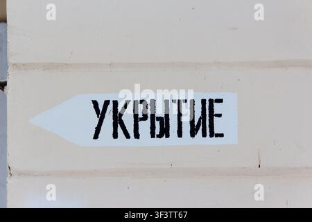 Directional sign for a shelter in Russian painted on a beige building wall, showing a black arrow pointing the way to safety during an emergency situa Stock Photo