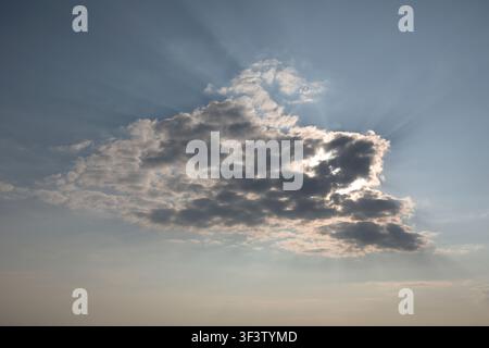 A blue, cloudy sky with the sun shining through from behind the clouds Stock Photo