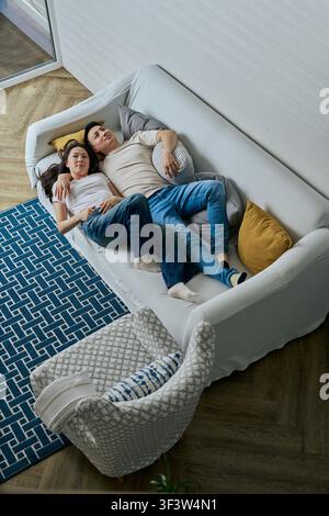 Overhead view of a man and woman relaxing together on a sofa in a cozy living room, lounging with pillows and blankets, enjoying quiet time at home. Stock Photo