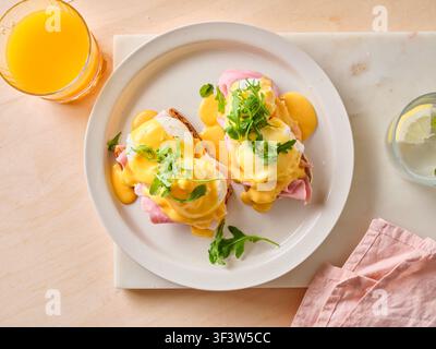 A delectable brunch spread featuring classic egg benedict with poached eggs and hollandaise sauce on a toasted bread, garnished with greens and served Stock Photo