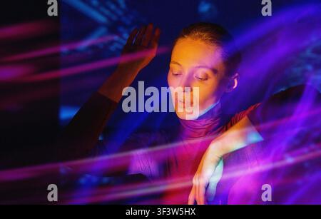 Portrait of a woman immersed in virtual reality, bathed in neon purple and blue light trails, exploring a futuristic digital space with a calm, focuse Stock Photo