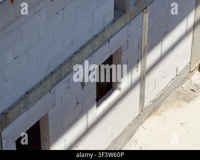 Close-up of an unfinished wall made of white aerated concrete blocks with rough mortar joints and window openings, captured in sunlight at a building Stock Photo