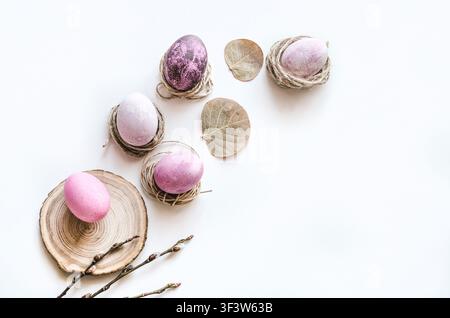 Minimal pastel Easter flat lay with colored eggs in twine nests, dried leaves, and a wood slice on a bright white background, offering clean copy spac Stock Photo