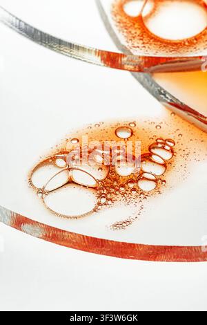 High-key macro photo of amber-colored oil bubbles floating in a clear liquid on a glass surface, creating an abstract texture on a white background. Stock Photo