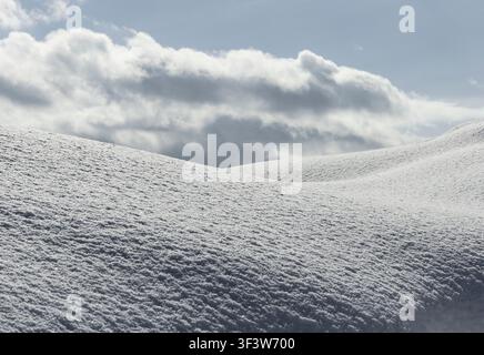 A close view of textured powder snow forming soft rolling drifts beneath a cloudy winter sky in Hokkaido, Japan, creating a calm abstract landscape of Stock Photo