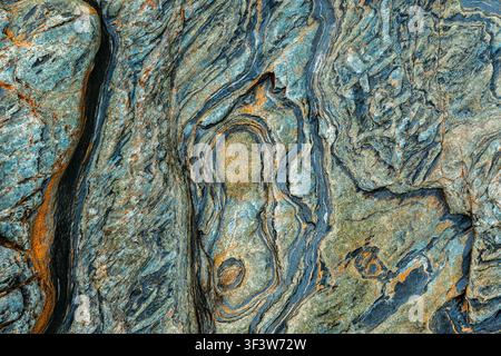 Detailed close-up of metamorphic rock texture with swirling blue-gray layers and rusty veins, forming a natural abstract stone background for design, Stock Photo