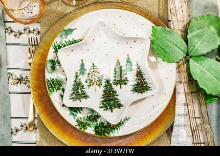 Overhead view of an elegant Christmas dinner table setting with a star-shaped plate, tree motif tableware, gold charger, cutlery, and seasonal holiday Stock Photo
