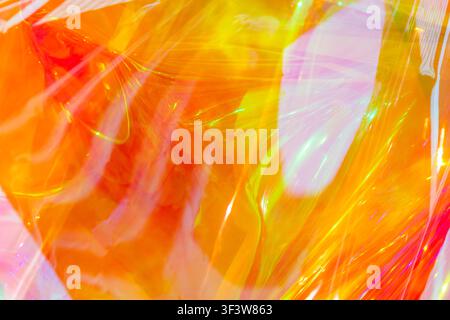 Abstract image featuring vibrant holographic waves in shades of orange, yellow, and pink. The bright, shiny surface resembles a flowing rainbow with d Stock Photo
