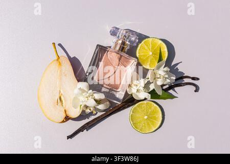 Elegant flat lay of a pink perfume bottle styled with sliced pear, lime halves, white jasmine blossoms and vanilla pods on a bright background with cr Stock Photo