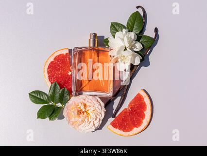 Flat lay of elegant perfume bottle surrounded by grapefruit slices, rose and jasmine flowers, green leaves and vanilla pods on a clean light backgroun Stock Photo