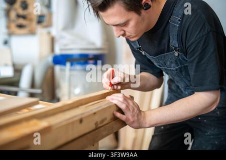 Pensive man woodworker in carpentry preparing materials before old window frame restoration. Stock Photo