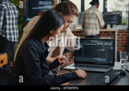 Software development team reviews laptop source code at a desk in a server room, collaborating on artificial intelligence, database work and a coding project. Stock Photo