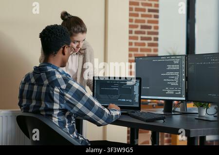Two programmers give a high five at a desk with multiple screens running code, celebrating a successful algorithm and teamwork result in an IT agency. Stock Photo