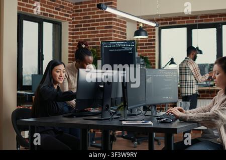 Software engineer types source code at a computer keyboard while colleagues join a group project in an IT startup office during a coding workflow. Stock Photo