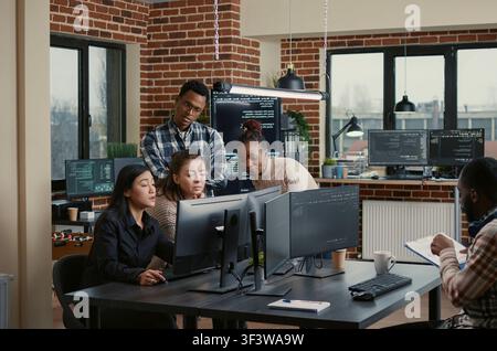 Software team discusses code feedback together while a developer team discusses algorithms, database work and new software ideas across office computer screens. Stock Photo