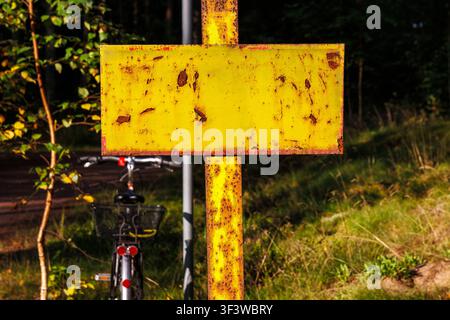 Closeup of a rusty blank yellow metal sign mounted on a corroded pole beside a forest road in Finland. Stock Photo