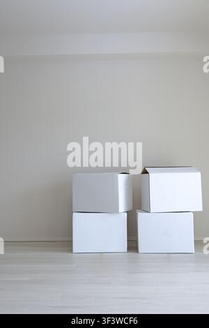 White cardboard boxes stacked against a wall in a bright room Stock Photo