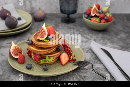 Breakfast stack topped with fresh figs, strawberries and berries styled on moody grey background Stock Photo