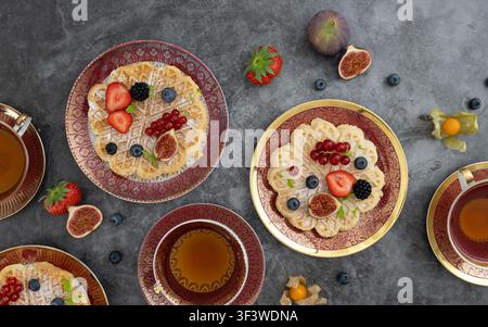 Top view composition of pancakes, berries, figs and tea arranged on textured grey background Stock Photo