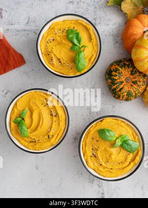 Top view food photography of three bowls of smooth pumpkin soup styled with seasonal squash and fresh basil Stock Photo