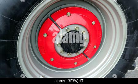 Close view of a large tractor wheel highlighting the shiny red hub and metal bolts that secure the tire to its rim. This wheel is designed for heavy-d Stock Photo