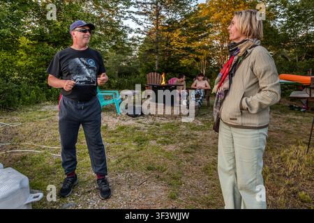 Timothy Doucette and Angela Berg on the grounds of the Deep Sky Eye Observatory on Frotten Road near Tusket, Nova Scotia, Canada. In the background, two teenagers are sitting by the fire as dusk falls – visitors gather here before the start of the nightly observatory tour Stock Photo