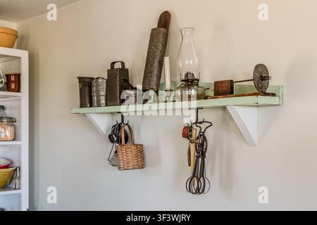 Antique kitchen utensils, such as a grater, a rolling pin, a whisk and a paraffin lamp, hang on a wall shelf in a historic farmhouse at the Le Village historique acadien de la Nouvelle-Écosse on Old Church Road in Lower West Pubnico, Nova Scotia. The items illustrate the kitchen equipment found in Acadian households around 1900. Argyle Municipal, Nova Scotia, Canada Stock Photo
