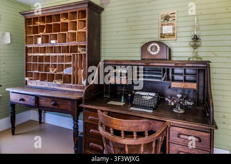 A mechanical typewriter stands on a roll-top desk next to a postbox rack in the replica post office building at the Le Village historique acadien de la Nouvelle-Écosse on Old Church Road in Lower West Pubnico, Nova Scotia. The interior of the ‘Bureau de Poste’ depicts the workplace of a rural postmaster around 1900. Argyle Municipal, Nova Scotia, Canada Stock Photo