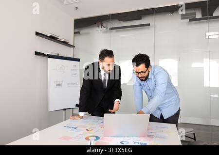 Two male professionals discussing business documents, working on laptop Stock Photo